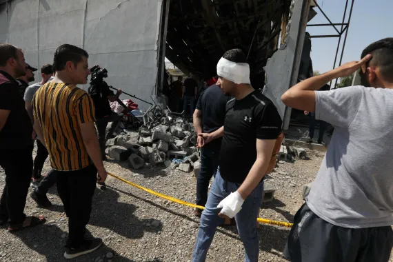 An injured man walks among people assessing the damage in front of the cordoned-off event hall [Safin Hamid/AFP]